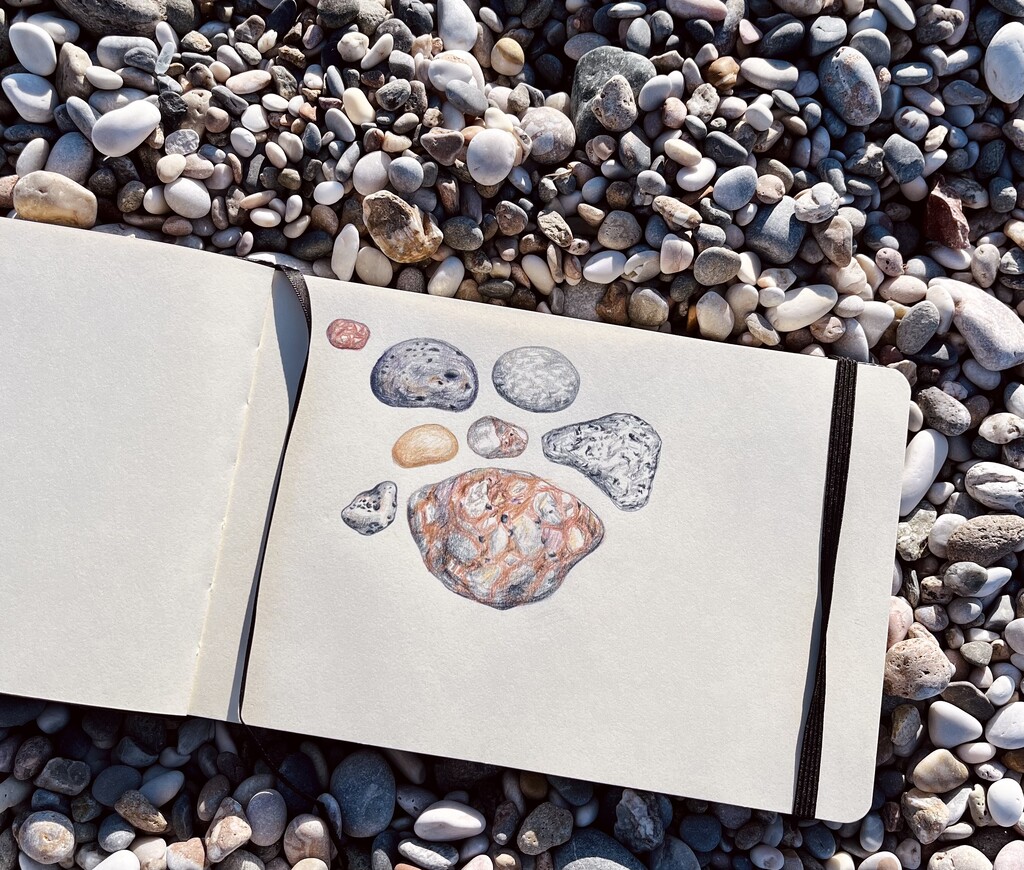 A sketchbook showing a sketch of colorful pebbles laying on the beach.